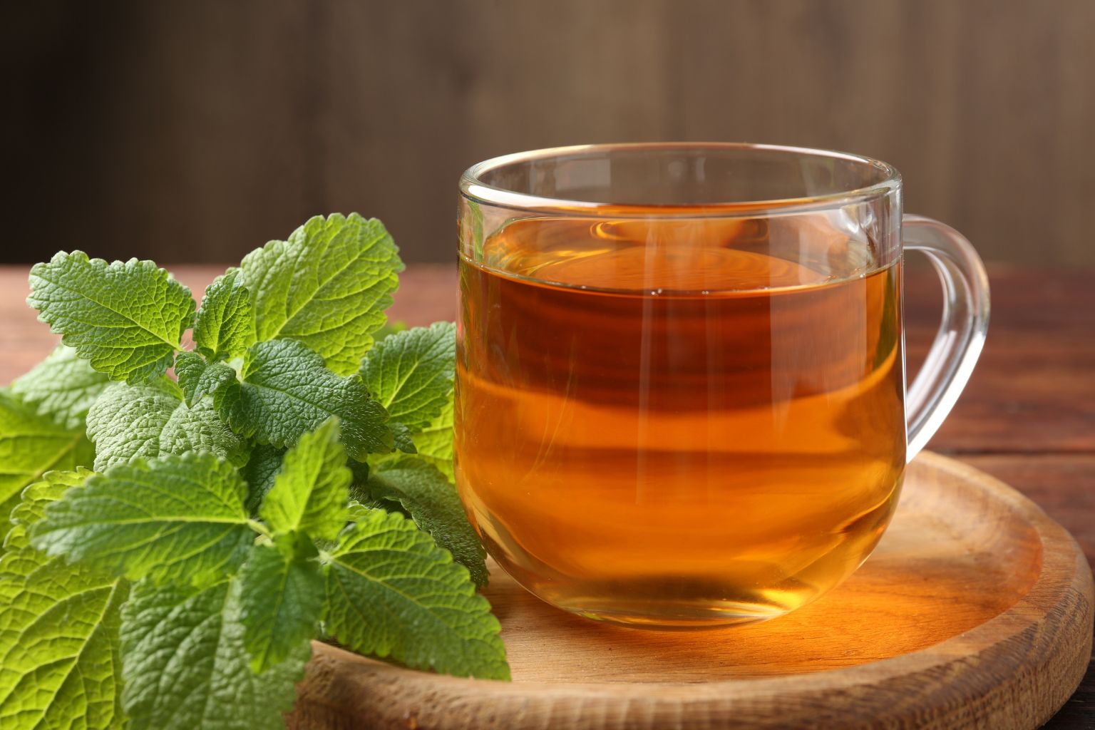 Tisana di melissa in tazza trasparente con foglie essiccate accanto.